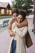 © LIGHTFIELD STUDIOS - smiling man embracing happy african american girlfriend near building outdoors.