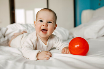 five months old baby lying on stomach, laughing, playing with a red ball.