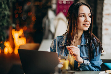 Young female student working on laptop in bar and eating pizza