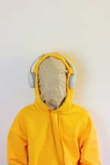 Wall Mural - unknown person with a paper mask on his face in a yellow sweatshirt with a hood on his head and headphones close up