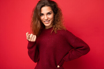 Young beautiful self-confident curly brunette woman with sincere emotions poising isolated on background wall with copy space wearing casual dark red sweater. Positive concept