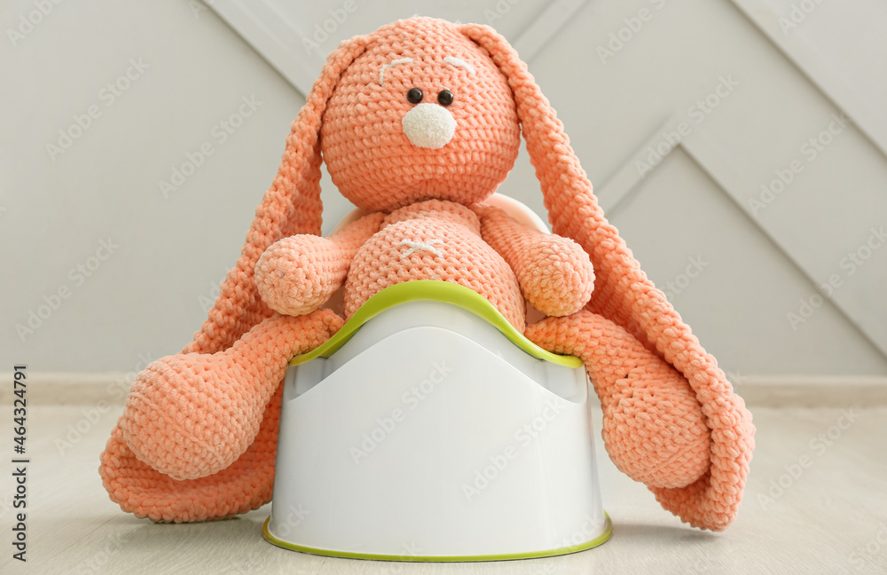 Cute toy hare sitting on potty near grey wall