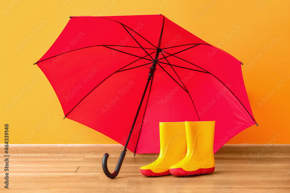 Pair of rubber boots with umbrella near color wall