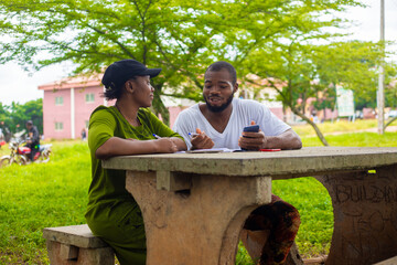 Wall Mural - Black university handsome man assisting his female friend with her lecture in the campus. Focus is on student.