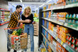 © Zamrznuti tonovi - Couple in supermarket using smartphone with shopping cart while grocery shopping