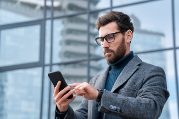 Wall Mural - businessman using mobile app standing outside office in urban city street