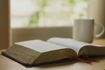 Wall Mural - Close up of open bible with a cup of coffee for morning devotion on wooden table with window light. Christian background.