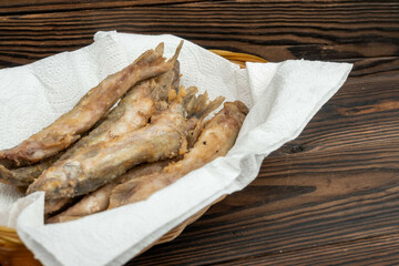 Fried fish on a paper napkin in a wicker basket on a wooden table.