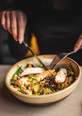 Young woman hand eating donburi with chicken and rice using knife and fork fom bowl