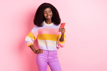 Wall Mural - Portrait of charming positive dark skin girl put arm on waist look phone isolated on pink color background