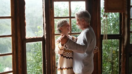 Wall Mural - Happy senior couple smile and dance at home enjoying love and relationship together. Active old man and woman have fun in indoor leisure activity. Nature woods view from windows