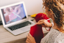 Young Woman Knitting Wool Using Needle While Watching Online Tutorial On Laptop At Home. Woman Watching Needlework Lessons On Laptop. Caucasian Woman Learning To Knit Online.