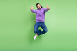 © deagreez - Full size photo of cool young brunet guy jump show thumb up wear hoodie jeans sneakers isolated on green background