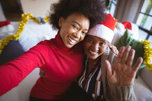 Smiling African American Adult Daughter And Senior Mother In Santa Hats Taking Christmas Selfie