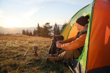 Wall Mural - Man with cup of hot drink in camping tent. Space for text