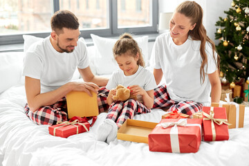 Sticker - family, winter holidays and people concept - happy mother, father and little daughter opening christmas gifts in bed at home