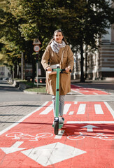 Wall Mural - traffic, city transport and people concept - woman riding electric scooter along red bike lane with signs of bicycles and two way arrows on street