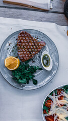 Wall Mural - Top view shot of a plate with tuna steak, a sauce, greens, and a lemon on the side