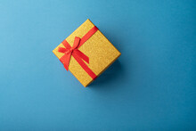 Red And Gold Gift Box With A Red Ribbon On A Light Blue Background
