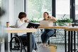 © LIGHTFIELD STUDIOS - businesswoman in wheelchair showing notebook to african american colleague pointing at laptop