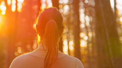 Wall Mural - CLOSE UP: Golden sunbeams shine on brunette woman going for a walk in forest.