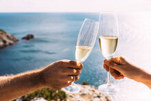 Hands Holding Champagne Glasses Over The Sea. Romantic Vacation. Two Hands Holding Champagne Glasses On The Background Of The Sea. Toast With Champagne Glasses On The Seashore. Copy Space