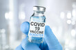 Hand in blue medical gloves holding a vaccine vial with Covid 19 Vaccine Booster text, for Coronavirus booster shot.