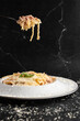 Pasta Carbonara on fork isolated. Spaghetti with bacon, parmesan, cream sauce and egg yolk on black marble background. Mediterranean gourmet food.