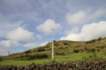 Wall Mural - Shot of a transmission pole above a stone wall in a field with sky in the background