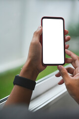 Poster - Photo of a woman hand with a digital watch holding a white blank screen smartphone over the window sill as a background.