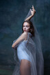 Close-up of young beautiful girl, ballerina posing with white transparent cloth isolated on dark vintage studio background.