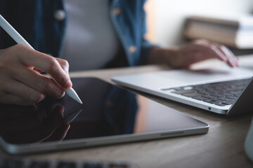 Poster - Close up of business woman hand with stylus pen working on digital tablet pc and laptop computer on office table at home