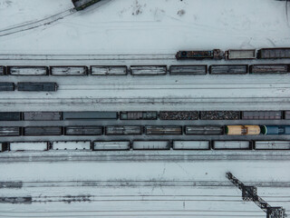 Aerial view of freight trains at the train station. Wagons with goods by rail. Heavy industry. Industrial concept scene with trains. View from a flying drone. winter landscape