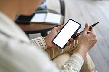 Poster - Top view image of a smart man holding a pen and using a white blank screen smartphone while sitting at the wooden vintage chair.