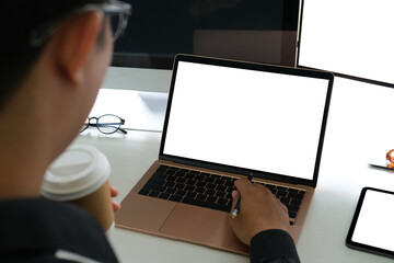 Poster - Behind view of a businessman holding a coffee cup while using a white blank screen computer laptop at the working desk.