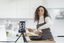 Latin Women Live Streaming Online With A Smartphone While Cooking In The Kitchen At Home.