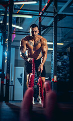 Front view of young man, muscled athlete, bodybuilder training alone at sport gym, indoors. Concept of sport, activity, healthy lifestyle