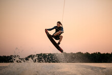 Active Strong Man Making Trick In Jump Time With Wakeboard On Sky Background.