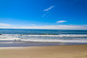 a beautiful shot of miles of vast blue ocean water and waves rolling into a beach with silky brown sand with blue sky and clouds at Rincon Beach in Ventura County California USA