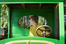 Boy With Autism Sitting In A Green Antique Car At A Pumpkin Patch; Child Looks Out Back Window While Hand Rests On The Steering Wheel