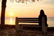 © Simeon - woman sitting alone on a bench at the beach in the autumn looking at the sunset