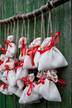 Christmas Advent Calendar Hangs On A Green Wooden Wall. Gift Bags Are Secured With Soutache Rope On A Wooden Branch. Closeup. Selective Focus
