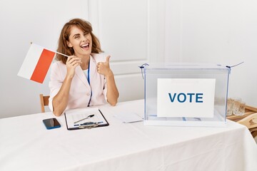 Canvas Print - Beautiful caucasian woman at political campaign election holding poland flag smiling happy and positive, thumb up doing excellent and approval sign