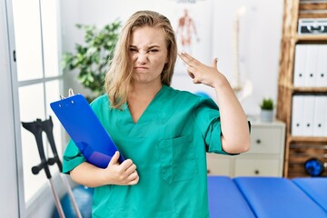 Poster - Young caucasian woman working at pain recovery clinic shooting and killing oneself pointing hand and fingers to head like gun, suicide gesture.