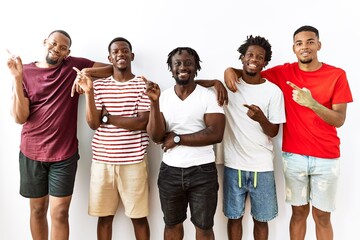 Canvas Print - Young african group of friends standing together over isolated background with a big smile on face, pointing with hand finger to the side looking at the camera.