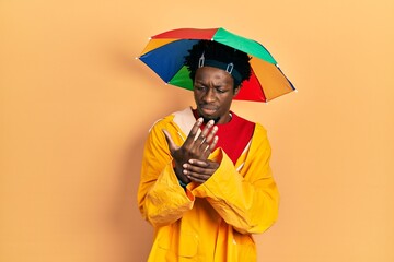 Poster - Young african american man wearing yellow raincoat suffering pain on hands and fingers, arthritis inflammation