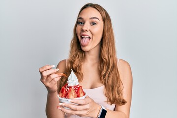 Sticker - Young blonde woman eating strawberry ice cream sticking tongue out happy with funny expression.