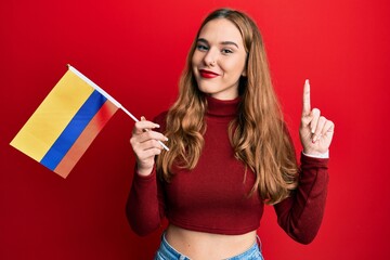 Sticker - Young blonde woman holding colombia flag smiling with an idea or question pointing finger with happy face, number one