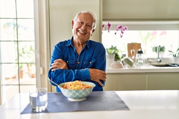 Sticker - Senior man with grey hair eating pasta spaghetti at home happy face smiling with crossed arms looking at the camera. positive person.