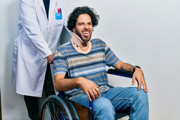 Poster - Handsome hispanic man sitting on wheelchair wearing neck collar sticking tongue out happy with funny expression. emotion concept.